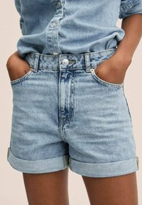 Pantalones cortos de mezclilla de color azul claro con cintura alta, puños enrollados, bolsillos frontales y un cierre visible de botón y cremallera. Patrón de desvanecimiento sutil.