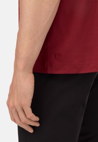 T-shirt corto bordeaux in cotone; presenta un piccolo logo ricamato vicino all'orlo e una superficie liscia, abbinato a pantaloni neri.