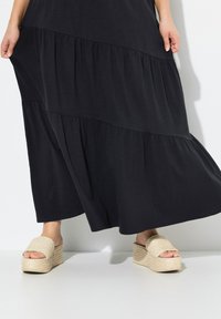 Abito maxi nero a strati realizzato in morbido tessuto, abbinato a sandali platform intrecciati color crema con suola spessa e design open toe.