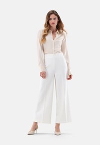 Light beige long-sleeve button-up shirt paired with high-waisted white wide-leg pants. Smooth fabric with a minimalistic design.