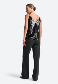 Čierny top na ramienka s flitrami a dizajnom V-zadnej časti, doplnený o vysoké šedé nohavice s širokým strihom. Hladká textúra, minimalistické ramienka, elegantný silueta.