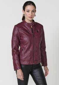 Veste en faux cuir bourgogne avec un col haut, des poches zippées et une texture côtelée sur les épaules. Associée à un pantalon noir texturé.