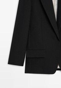 Czarna marynarka o strukturalnym kroju, z pojedynczą kieszenią na piersi, ostrymi klapami i gładką fakturą tkaniny.