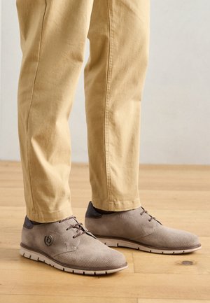 Chaussures marron clair en daim texturé avec un accent lisse marron foncé au niveau du talon, dotées de lacets plats et d'une semelle en caoutchouc pour une meilleure adhérence.