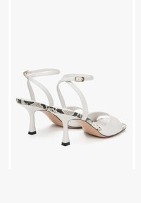 Witte sandalen met hakken en banden, met een geëtst slangenleerprint binnenzool, voorzien van een slanke blokhak met een zwarte basis en een verstelbare enkelband.