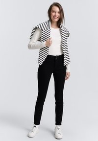 Sorte skinny jeans kombinert med en hvit langermet skjorte og en stripete oversized jakke, med bred krage og frontlommer.