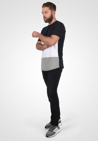 Camiseta bloqueada en colores negro, blanco y gris con mangas cortas, combinada con pantalones ajustados negros y zapatillas deportivas grises con acentos blancos.