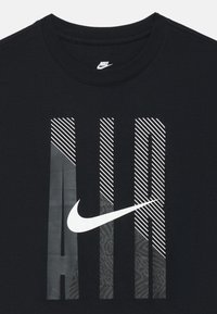 Čierne bavlnené tričko s odvážnym bielym nápisom "AIR" v rôznych vzoroch, vrátane pruhov a textúr, a s bielym logom Nike.