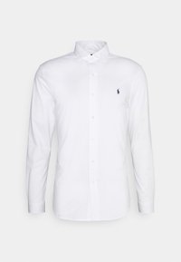 Witte, lange mouwen, katoenen overhemd met knopen. Voorzien van een spreidkraag, een knopenlijst aan de voorkant, en een klein marineblauw logo op de linkerborst.