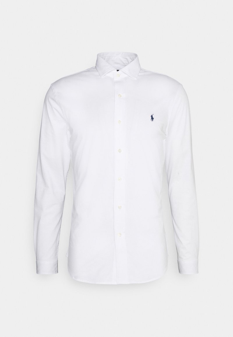 Witte, lange mouwen, katoenen overhemd met knopen. Voorzien van een spreidkraag, een knopenlijst aan de voorkant, en een klein marineblauw logo op de linkerborst.