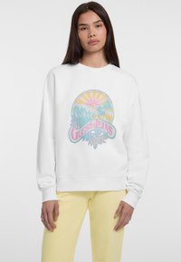 Sudadera blanca con un estampado gráfico colorido que presenta olas, palmeras y el texto "GUESS JEANS", con cuello redondo y puños acanalados.