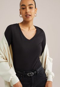 Juodas V-kaklo marškinėliai, lygus audinys, prigludęs dizainas, derinami su grietinėlės spalvos kardiganu su mygtukais. Juodas diržas su apvaliu sidabriniu sagtimi.