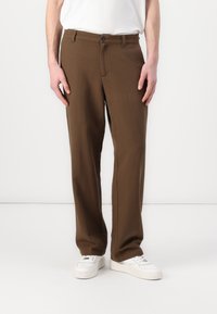 Brown trousers made of fabric with a straight-leg design. Features a front button closure and side pockets. Worn with white sneakers.