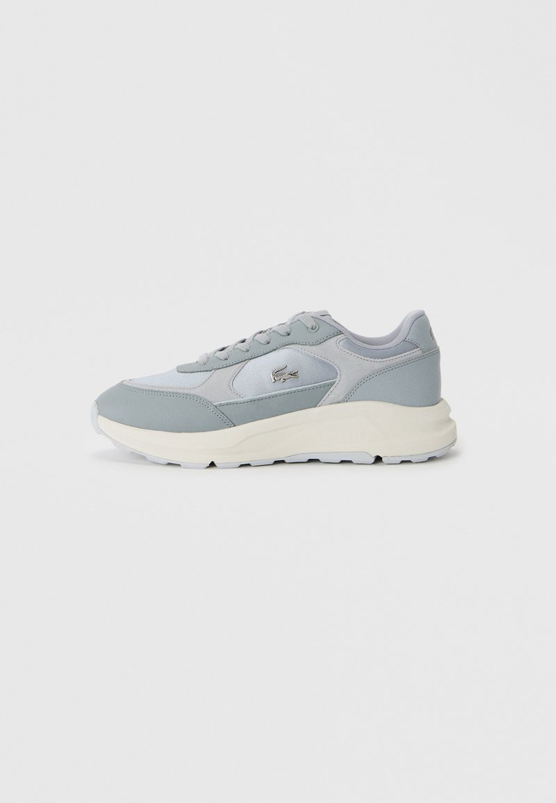 Sneaker Lacoste gris clair et blanc avec un laçage à l'avant, semelle rembourrée et logo crocodile brodé sur le côté, présenté de profil.