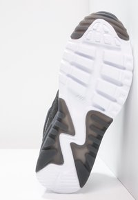 Svart sneakersula med texturerat vitt gummi, med en synlig varumärkeslogotyp och mönstrade spår för grepp.