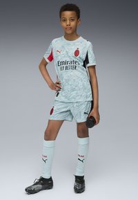 Jasnoniebieski strój piłkarski z marmurkowym wzorem. Czerwone i czarne akcenty, z logo. Czarne buty. Szorty i skarpetki do kolan dopełniają strój.