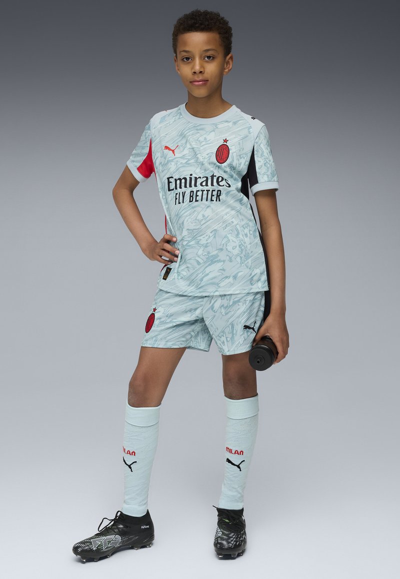 Jasnoniebieski strój piłkarski z marmurkowym wzorem. Czerwone i czarne akcenty, z logo. Czarne buty. Szorty i skarpetki do kolan dopełniają strój.