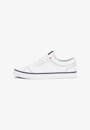 White canvas sneakers with a low profile, navy rubber outsole, red eyelets, and contrasting striped lining. Features logo on the side.