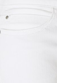 Tissu en denim blanc mettant en avant une vue rapprochée d'une poche avec des détails de couture subtils et un bouton métallique en accent.