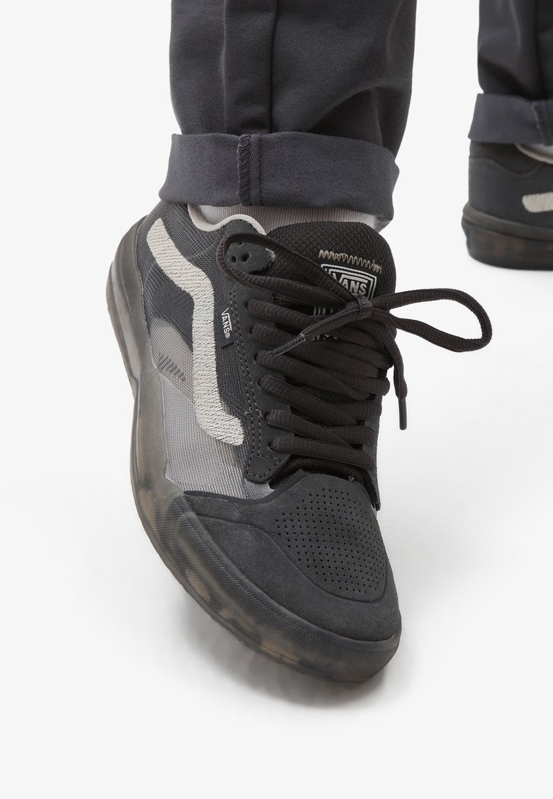 Baskets noires et grises en mesh et daim, avec languette rembourrée et fermeture à lacets. Elles présentent un logo visible et une semelle en caoutchouc.
