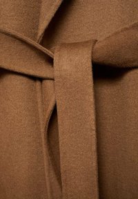 Brauner Wollmischgewebe mit weicher Textur, ausgestattet mit einem gebundenen Gürtel und sich überlappenden Frontklappen. Sichtbare Nahtdetails entlang der Kanten.