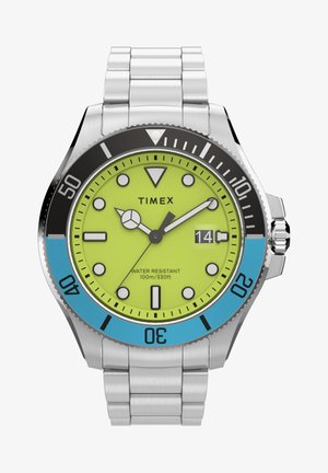 Timexi kell, millel on erksakollane kellaplaad, must ja sinine raam, roostevabast terasest rihm ning helendavad tunni numbrid. Veekindel kuni 100 m.