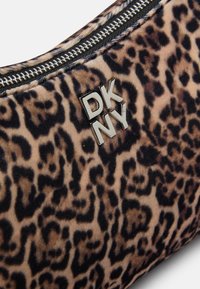 Torba z leopardjim vzorcem v mehkemu velurju, z srebrnim logotipom DKNY in črnima zadrgo na vrhu. Teksturni material z živahnimi vzorci.
