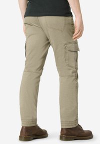 Beige cargo pants with multiple side pockets, textured fabric, and tapered design. Worn with brown boots, showing a straight leg cut.