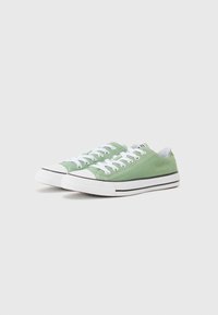 Grønne lærret sneakers med hvite snørebånd, gummifothette og sort aksentstripe langs sålen. Minimalistisk design og avrundet form.