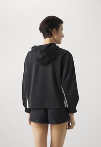 Sudadera negra con capucha y corte relajado, con acentos laterales blancos. Combinada con shorts negros texturizados, que capturan un aspecto deportivo.