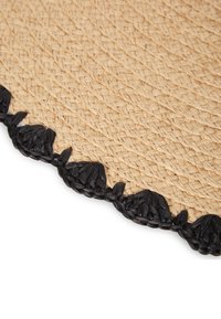 Tappeto intrecciato in paglia naturale con una superficie beige testurizzata e un bordo intrecciato nero con piccoli accenti a forma di foglia.