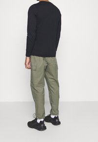 Svart långärmad skjorta, olivgröna cargobyxor, svarta sneakers med vita detaljer, visad bakifrån. Enfärgad tyg, avslappnad passform.