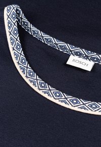 Navyblauwe kledingkraag met een decoratief geometrisch patroon in wit en blauw, benadrukt met een lichtbeige bies en een label met de tekst "RÖSCH."