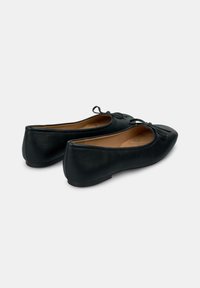 Bailarinas de cuero negro con punta afilada, pequeño detalle de lazo en la parte delantera y suela plana. Textura suave con un diseño elegante.