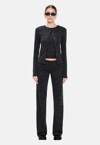 Completo in maglia nera a due pezzi con top corto aderente e cardigan lungo con bottoni, abbinato a pantaloni a gamba larga e scarpe nere.