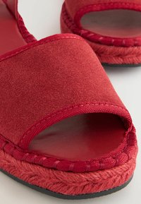 Rode suède espadrille sandalen met een open teen en gevlochten jute details rondom de zool. Gladde binnenvoering en platte rubberen buitenzool.