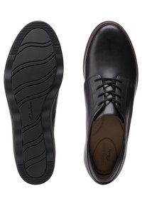 Chaussures habillées pour hommes en cuir noir à lacets, vues de dessus et de la semelle, présentant une finition lisse et une semelle en caoutchouc à motif ondulé.