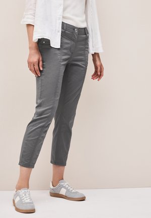 Pantaloni grigi a sigaretta con una texture liscia, chiusura frontale con bottone e tasche laterali. Abbinati a sneakers grigie e bianche.
