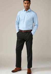 Camisa de botones de color azul claro con mangas largas, combinada con pantalones negros y zapatos de cuero marrón. Un cinturón marrón añade un detalle de contraste.