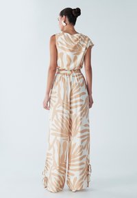 Robe maxi avec un motif de feuilles beige et blanc, dotée d'une taille cintrée et de manches courtes. Le tissu semble léger et texturé.