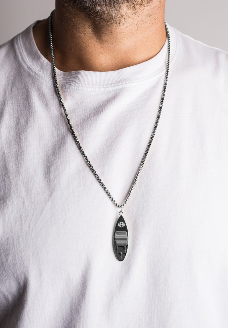 Zilveren ketting met een verlengd zwart hanger met een gemarmerd design en zilveren hardware accenten, gedragen over een witte shirt.