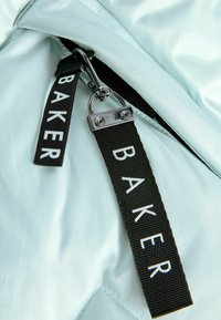 Tessuto trapuntato blu chiaro con tirazip nera che presenta la scritta "BAKER" in bianco. Texture liscia e finitura lucida con dettaglio in metallo della cerniera.