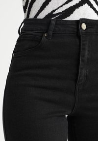 Svarta hög midja jeans med en slät yta, femfickorsdesign och metallknappstängning. Har subtila blekningar på låren.