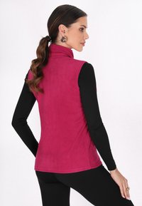 Vest din fleece de un roz vibrant, cu guler înalt, având o textură netedă și o siluetă ajustată, purtat peste un top negru cu mâneci lungi.