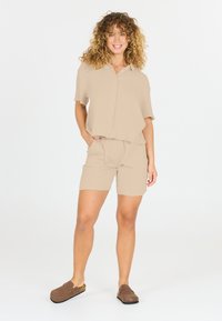 Beige matchande topp och shorts set, lättvikts texturerad tyg, korta ärmar, avslappnad passform, elastisk midja, i kombination med bruna slip-on skor.