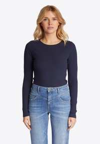 Top a maniche lunghe in maglia color navy, scollatura tonda, abbinato a jeans dritti leggeri blu chiaro con tasche frontali e dettagli di cucitura sottili.