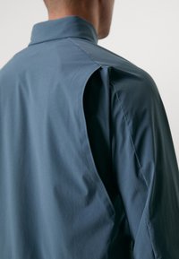 Blauwe, lichte shirt met een opgevouwen kraag en een hoekige snit op de schouder. Gladde textuur met zachte vallen.
