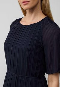 Robe plissée marine avec un col rond et des manches transparentes en volants, dotée d'une taille cintrée et d'un tissu lisse et fluide.