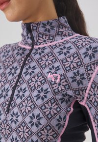 Quarter-zip topp med mønstret strikk i rosa og blått med svarte detaljer. Den har høy krage og en liten logo på brystet.
