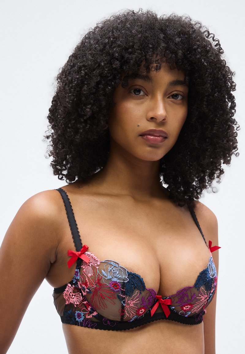 Schwarzer Spitzen-BH mit bunter Blumenstickerei in Pink und Blau. Mit roten Schleifenakzenten. Transparente Körbchen mit geschwungenen Kanten.